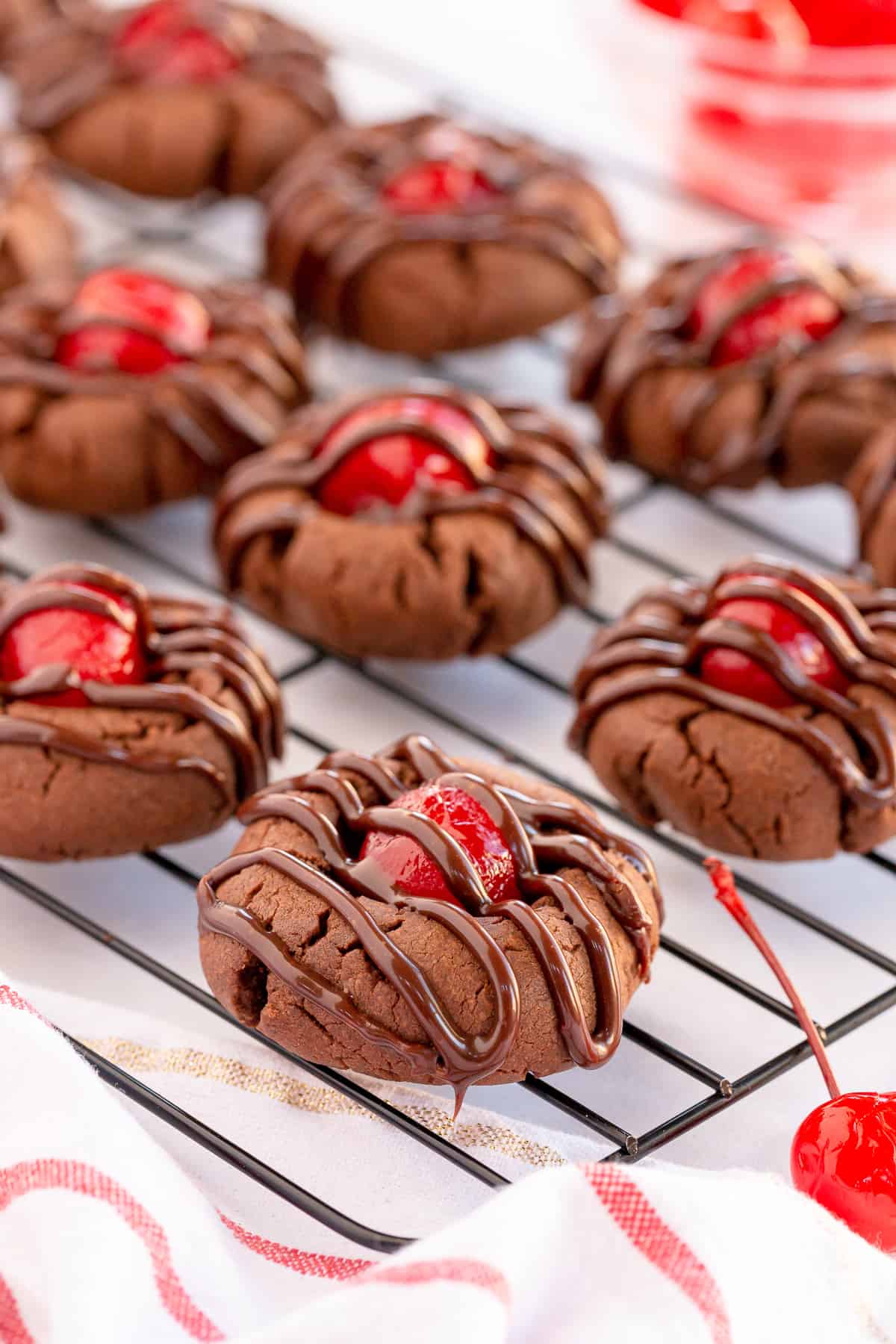 Chocolate cookies with maraschino cherries and frosting on a wire rack.