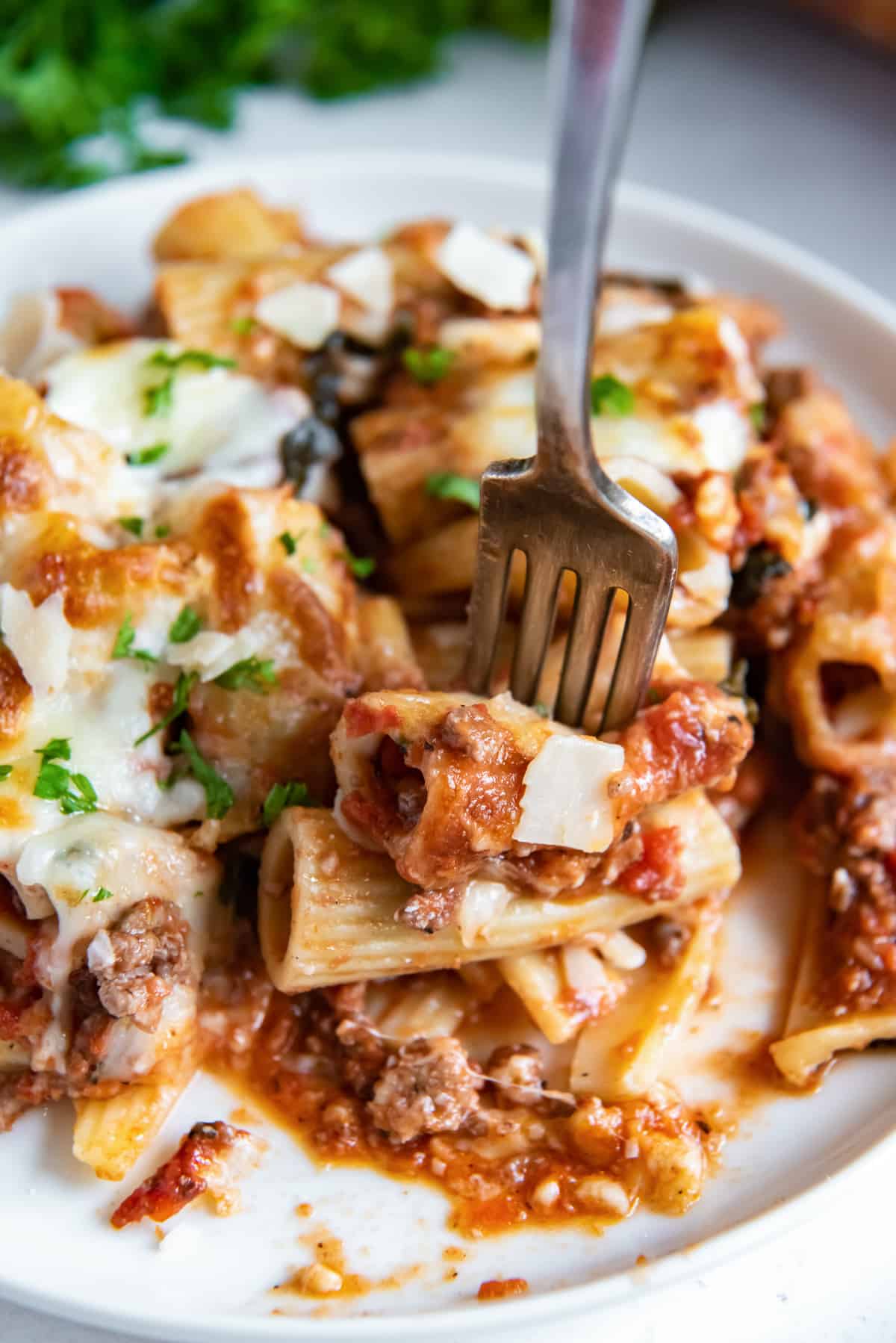A fork piercing into pieces of rigatoni on a dinner plate.