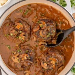 Salisbury steaks in a skillet with mushroom gravy.