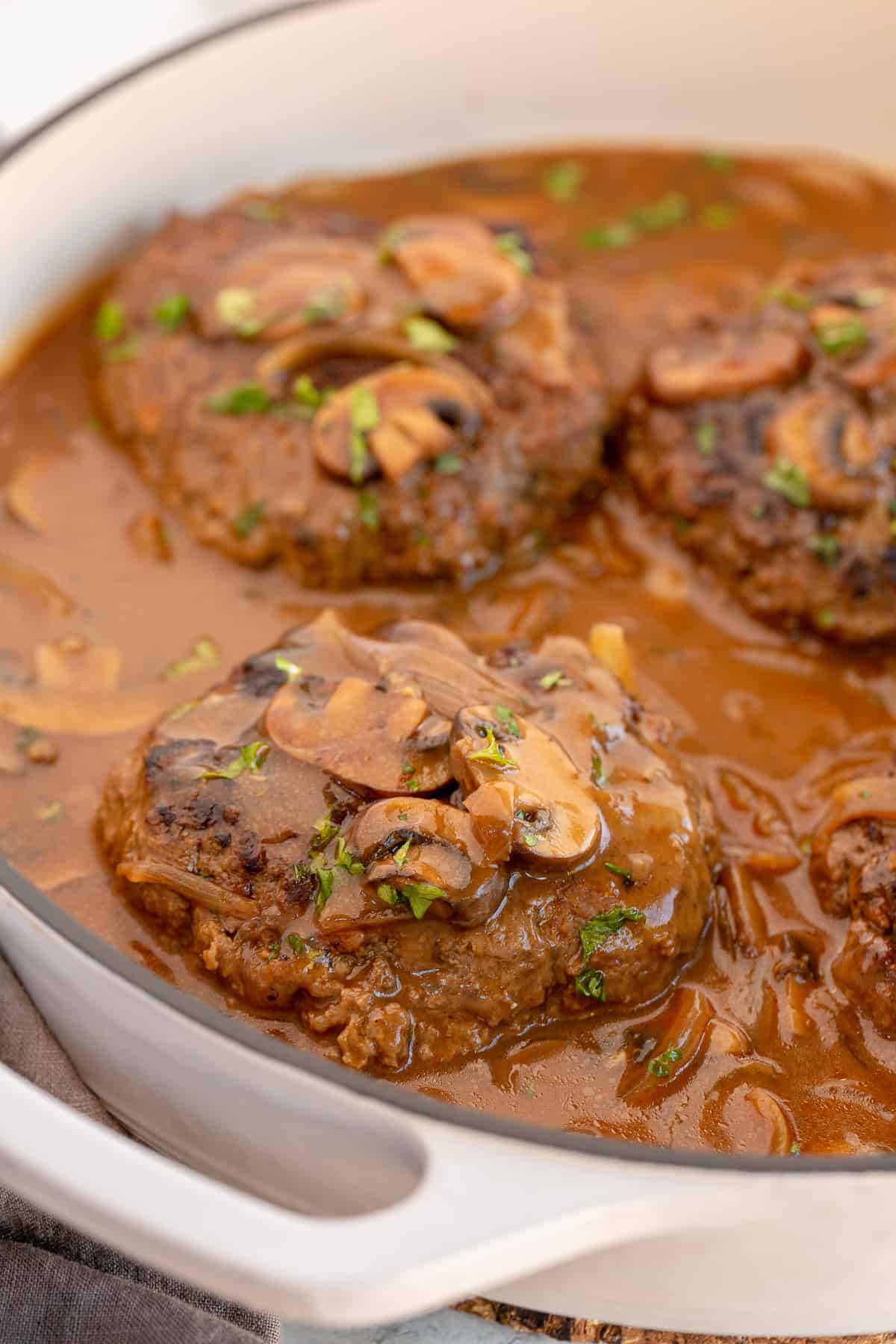 Salisbury steak in mushroom onion gravy in a white skillet.