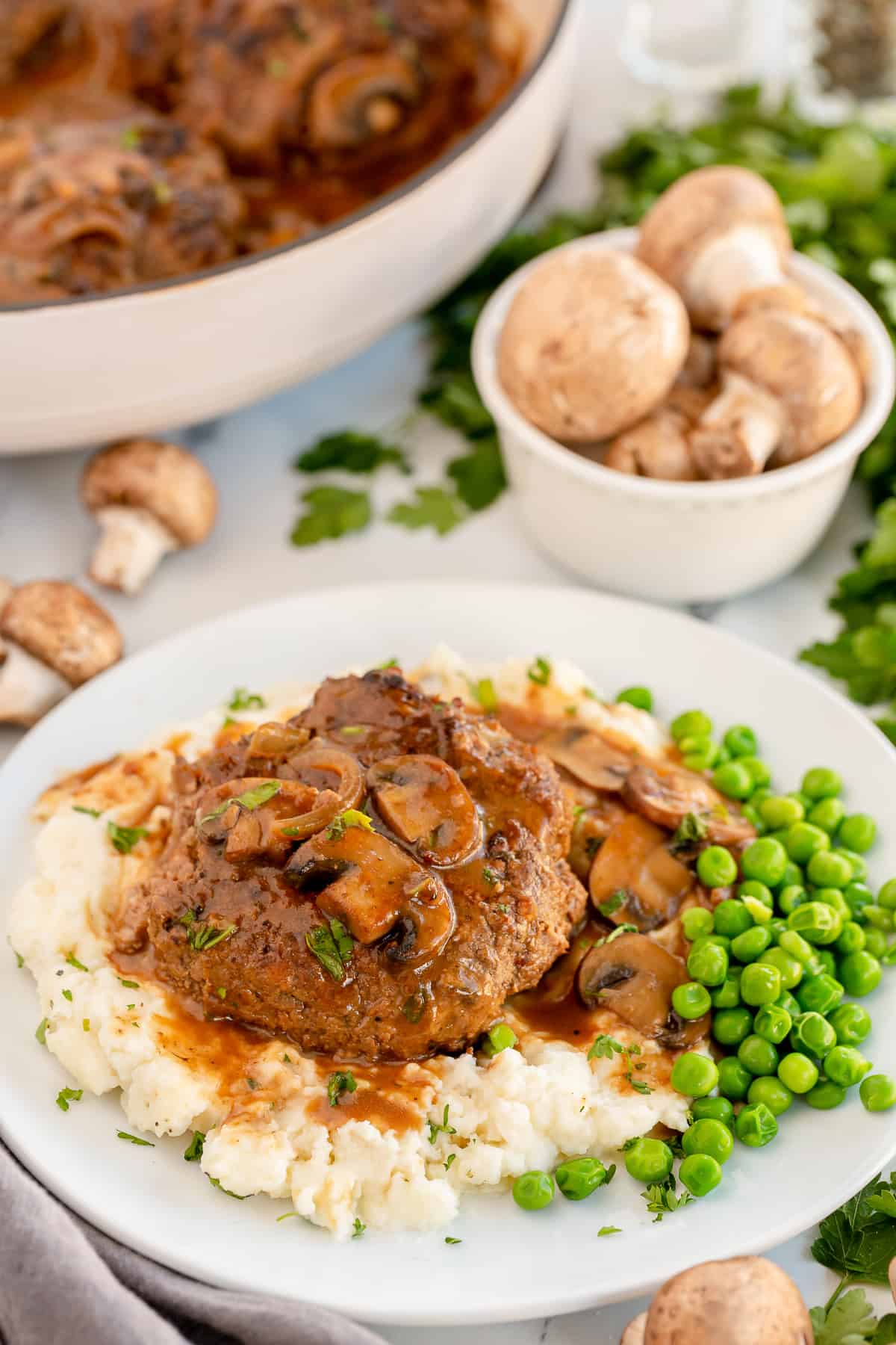 Salisbury steak and gravy on a plate with mashed potatoes and peas.