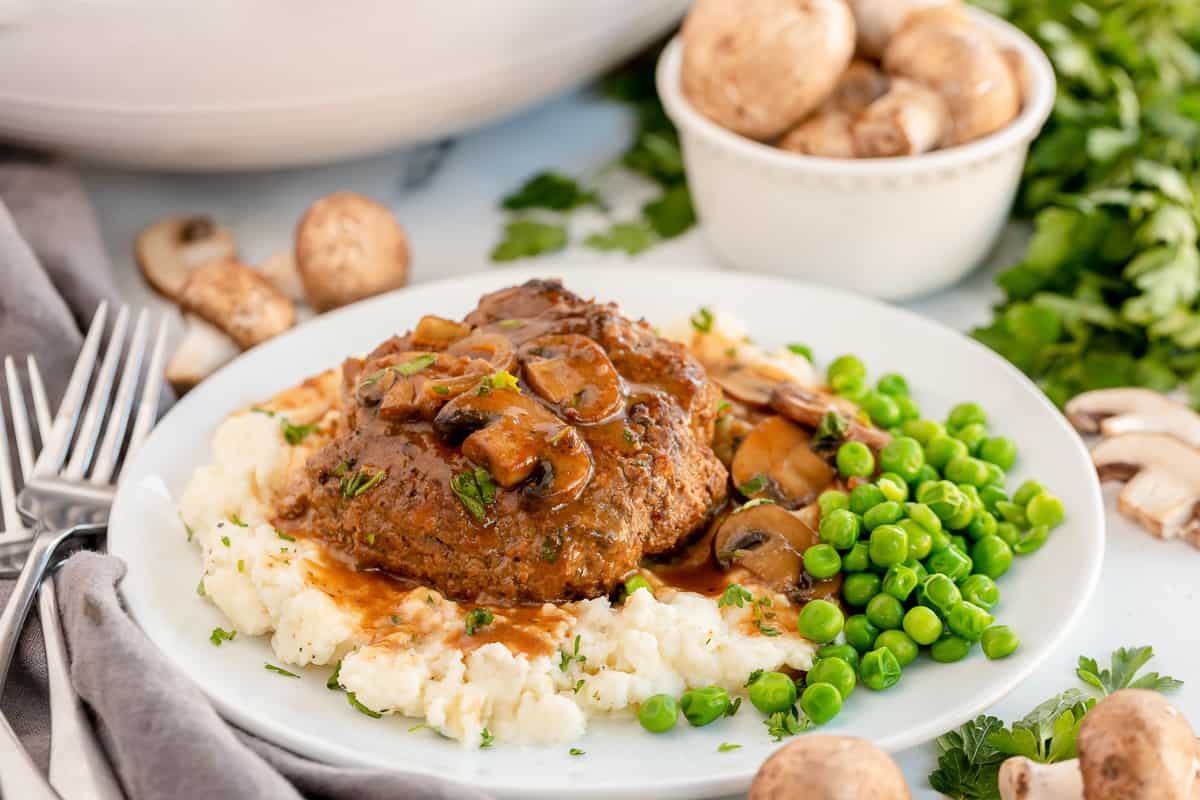 Salisbury steak on a plate with mashed potatoes and peas.