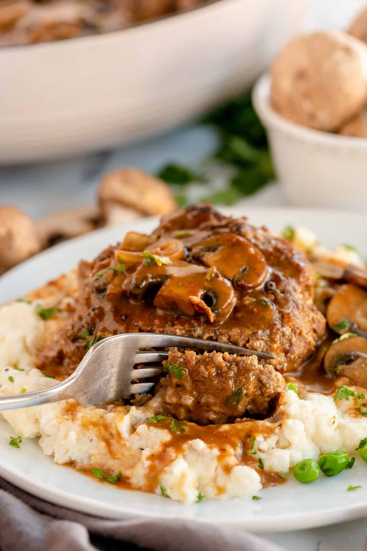 A fork breaking into a Salisbury steak on mashed potatoes.