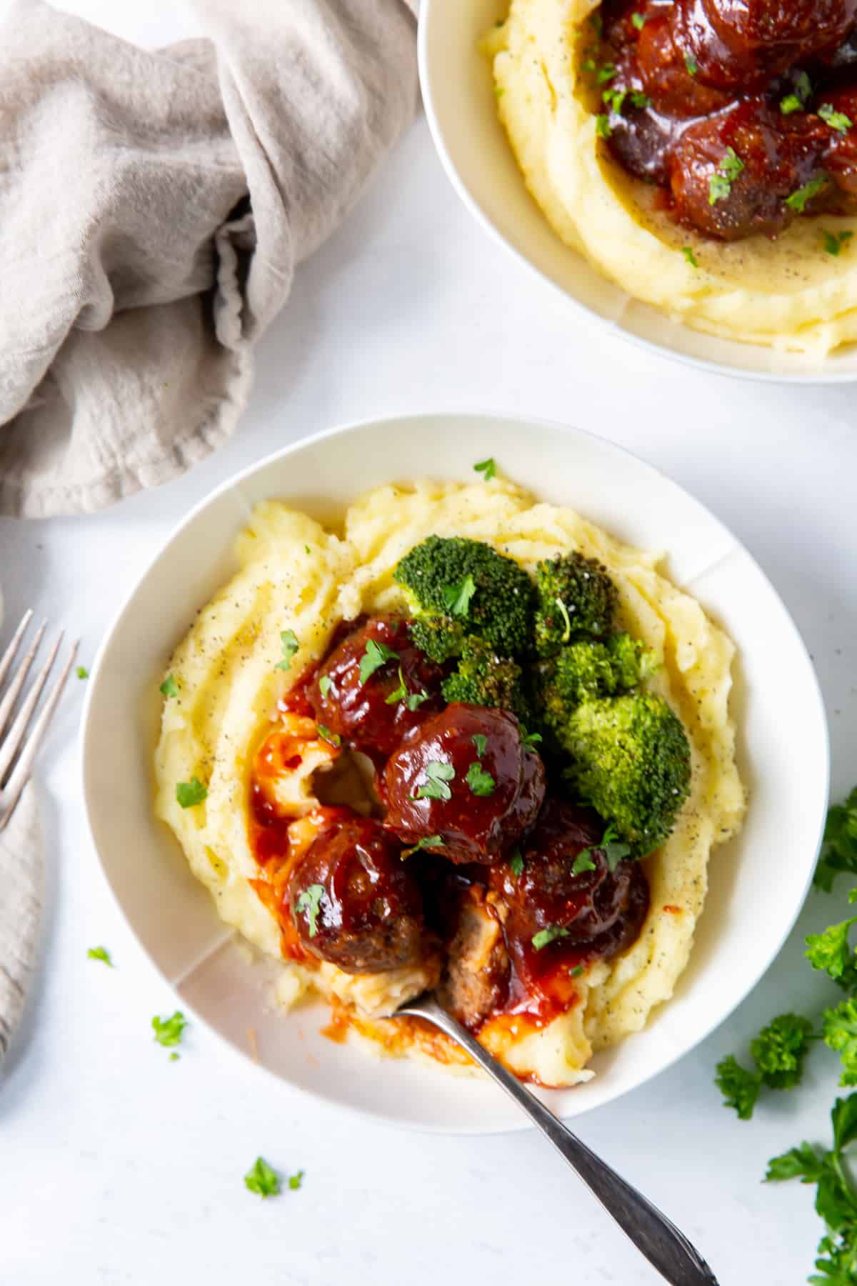 A top down shot of meatballs on mashed potatoes with broccoli.