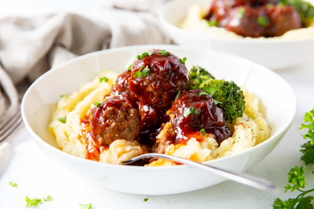 BBQ Meatballs over potatoes in a white bowl.