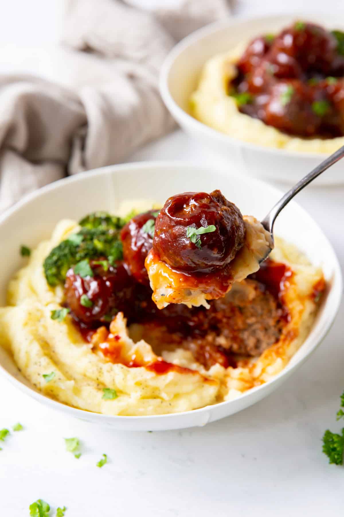 A fork lifts mashed potatoes topped with a BBQ meatball.