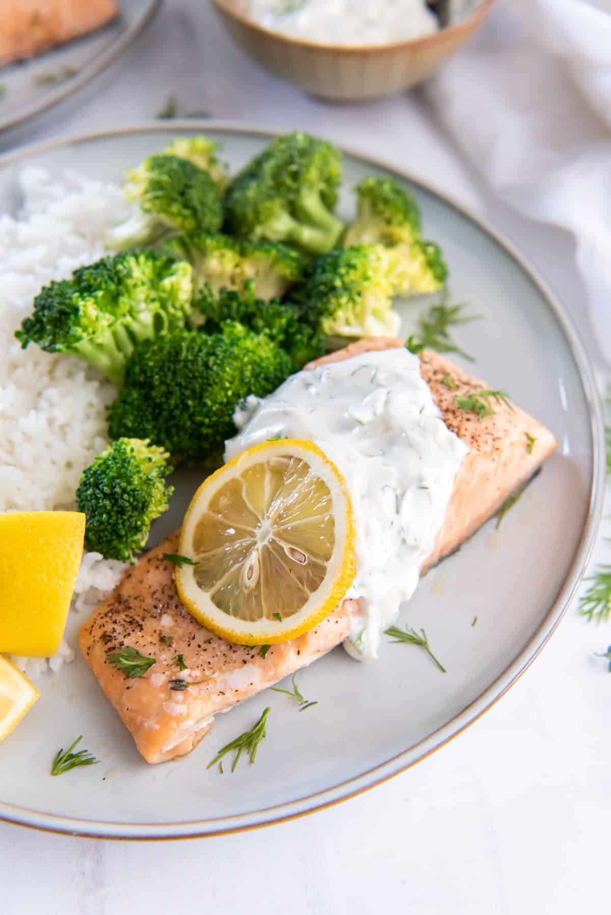 Salmon with dill sauce on a plate with broccoli and rice.