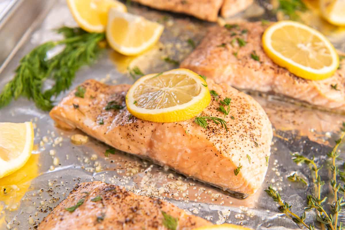 A salmon fillet topped with lemon and herbs on a baking sheet.