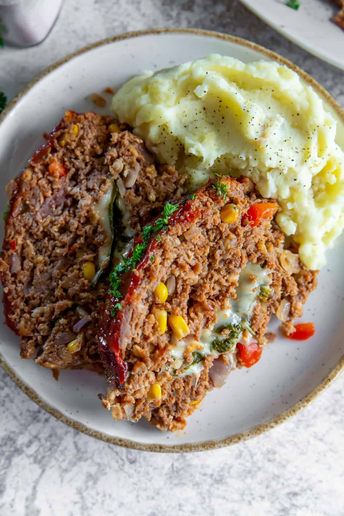 Two slices of cheese stuffed meatloaf on a plate with mashed potatoes.
