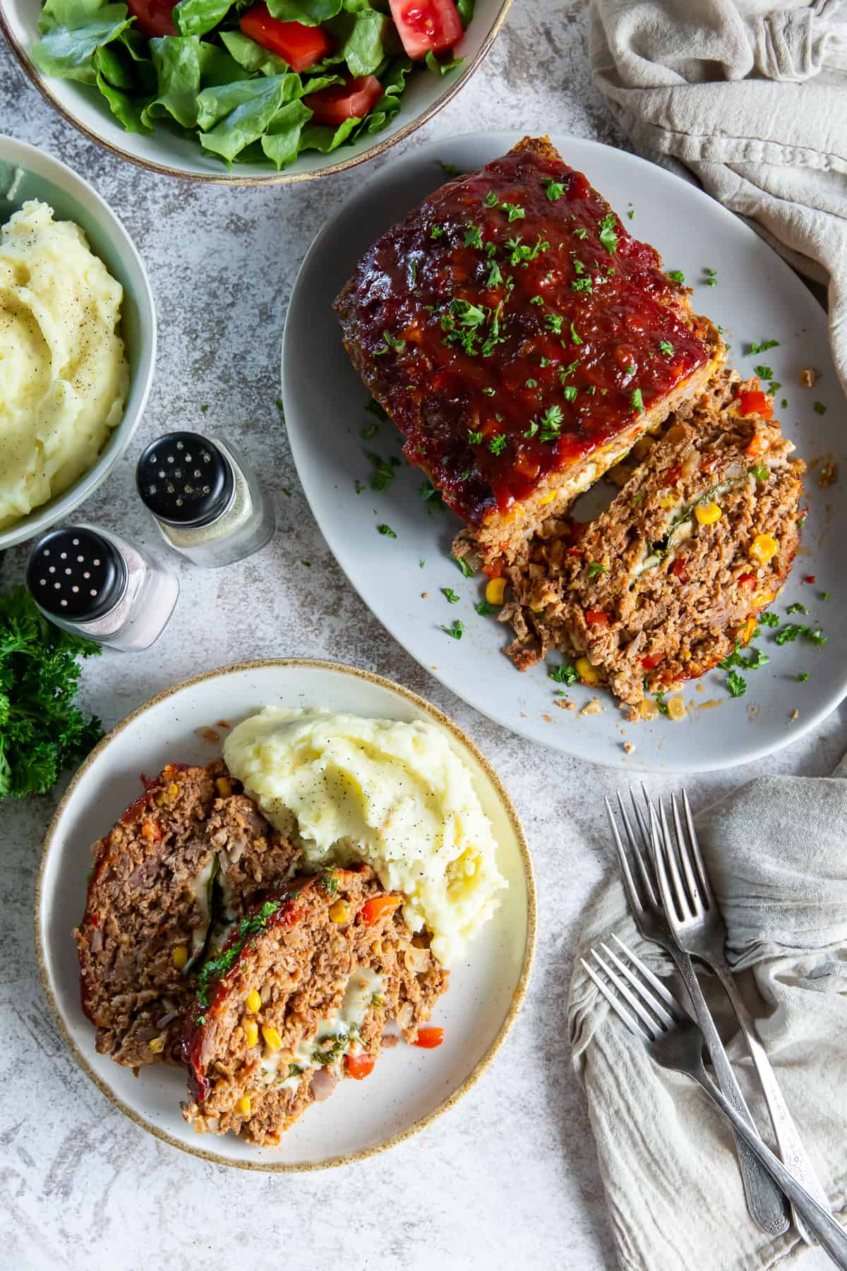An over the top shot of a meatloaf on a platter next to a dinner plate with mashed potatoes.