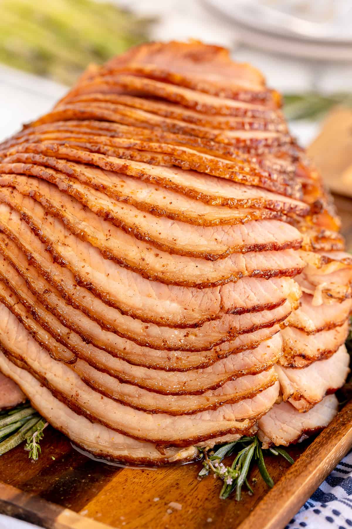 A baked spiral ham on a cutting board with fresh herbs.