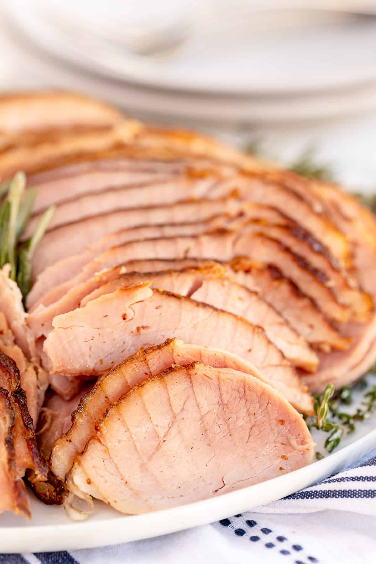 Sliced ham on a white platter with herbs.