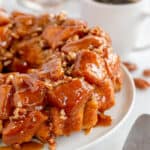 Monkey bread with pecans on a white plate next to a cup of coffee.