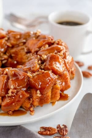 Monkey bread with pecans on a white plate next to a cup of coffee.