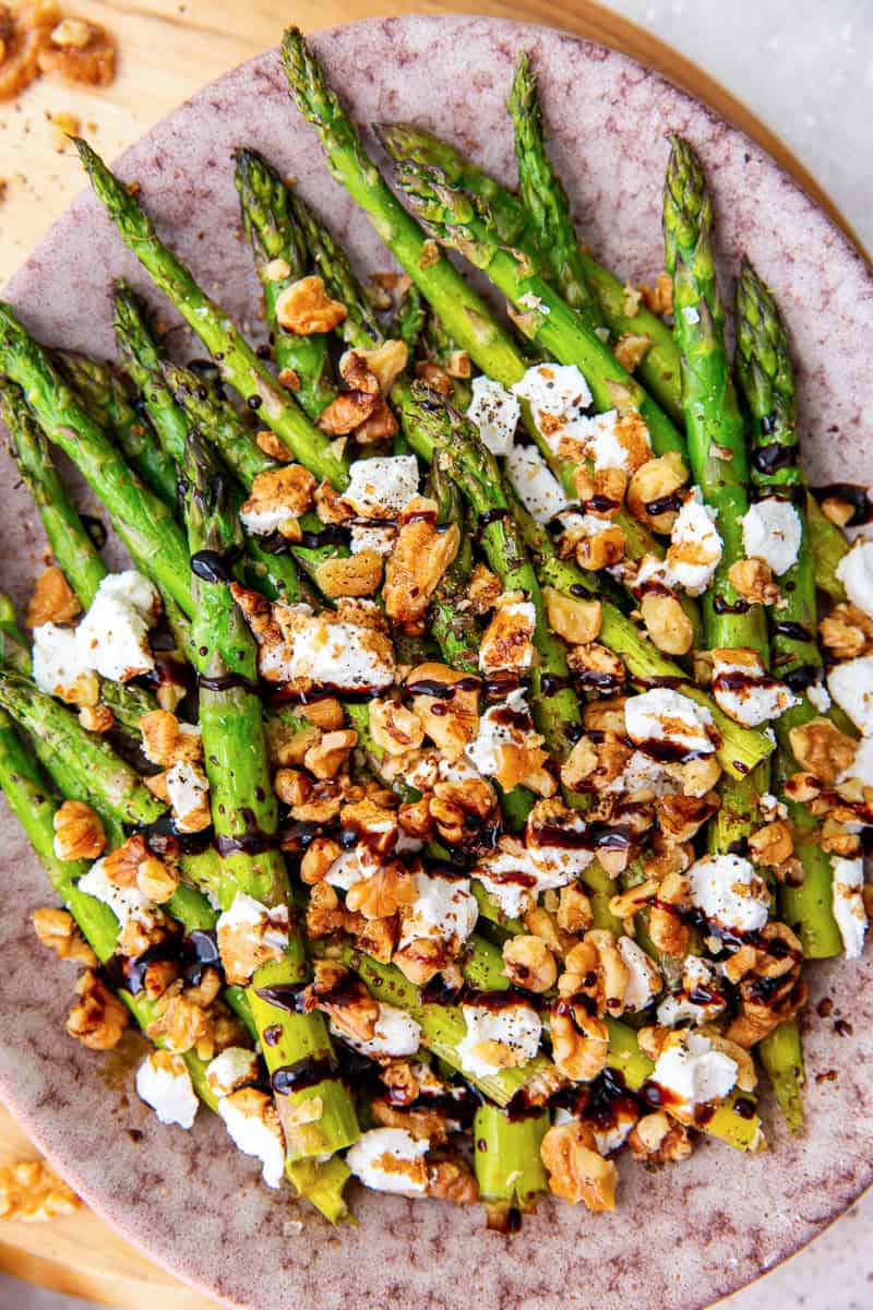 A top down shot of asparagus with balsamic and goat cheese on a pink platter.