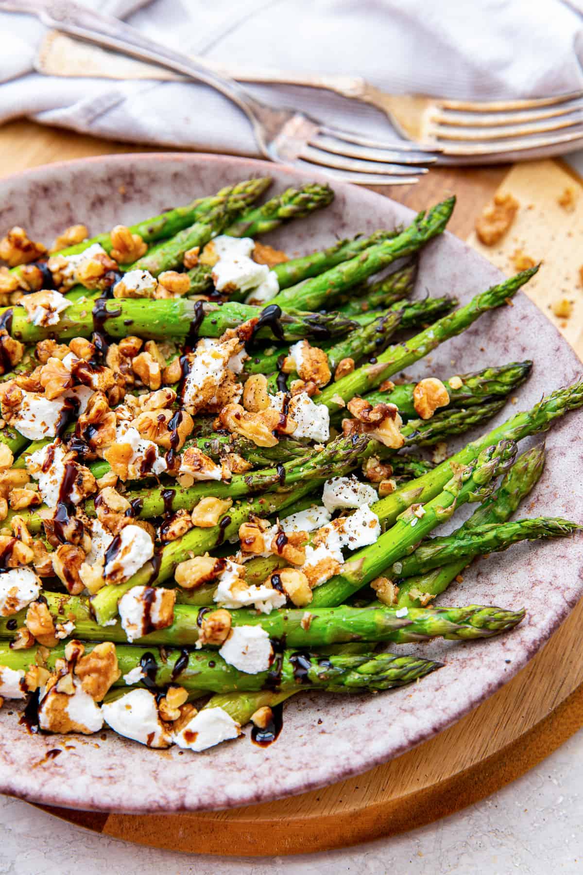 Asparagus with goat cheese and balsamic glaze on a pink plate.