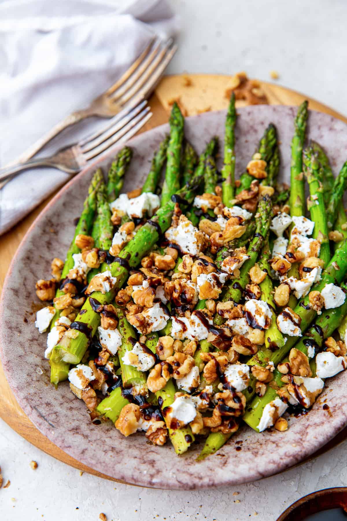 Roasted asparagus with goat cheese, walnuts, and balsamic on a platter.