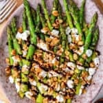 A top down shot of asparagus with balsamic glaze, goat cheese, and walnuts on a platter.