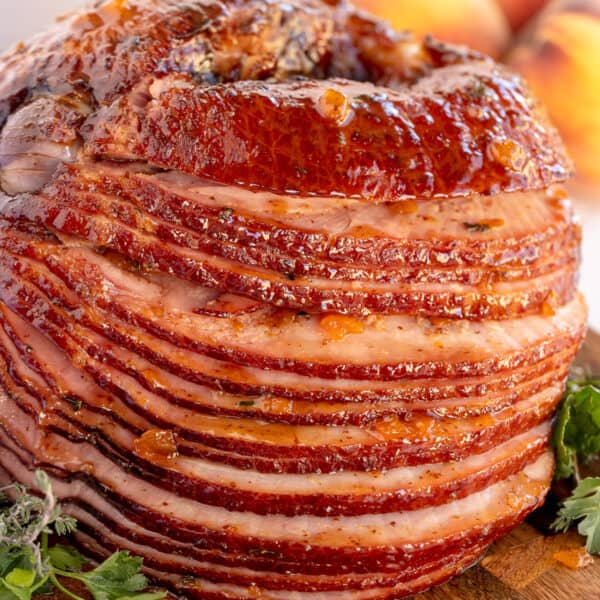 A spiral ham with peach thyme glaze on a wood board.