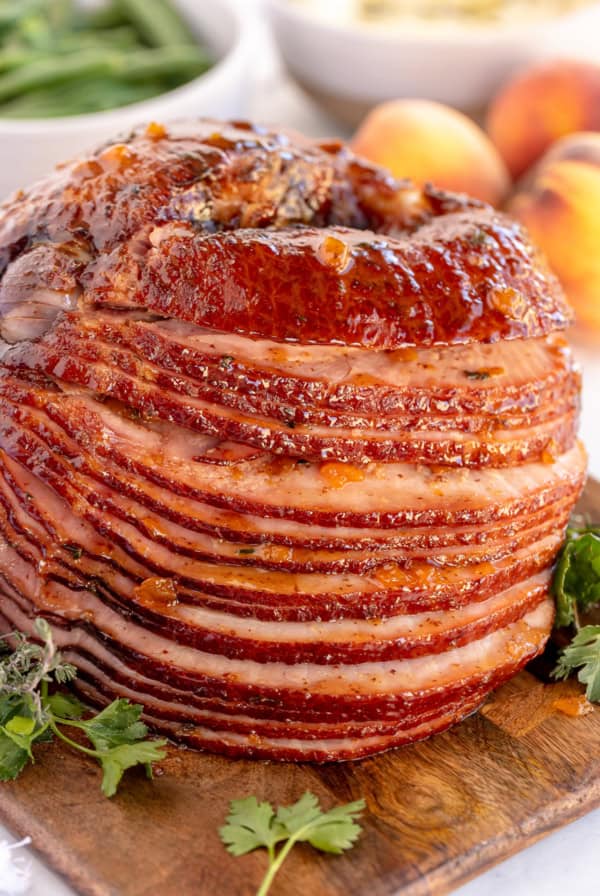 A spiral ham with peach thyme glaze on a wood board.