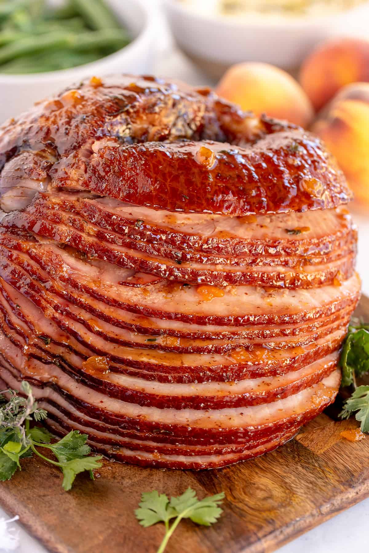 A slow cooked spiral ham with peach thyme glaze on a wood board.
