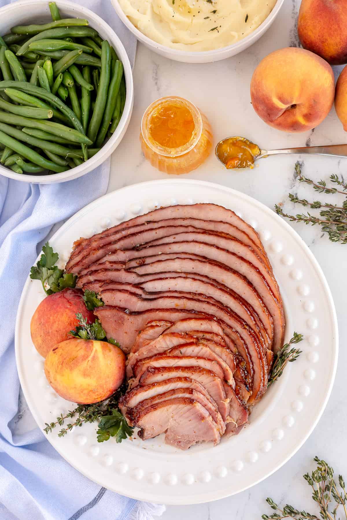 Sliced slow cooker ham on a platter with peaches and thyme.