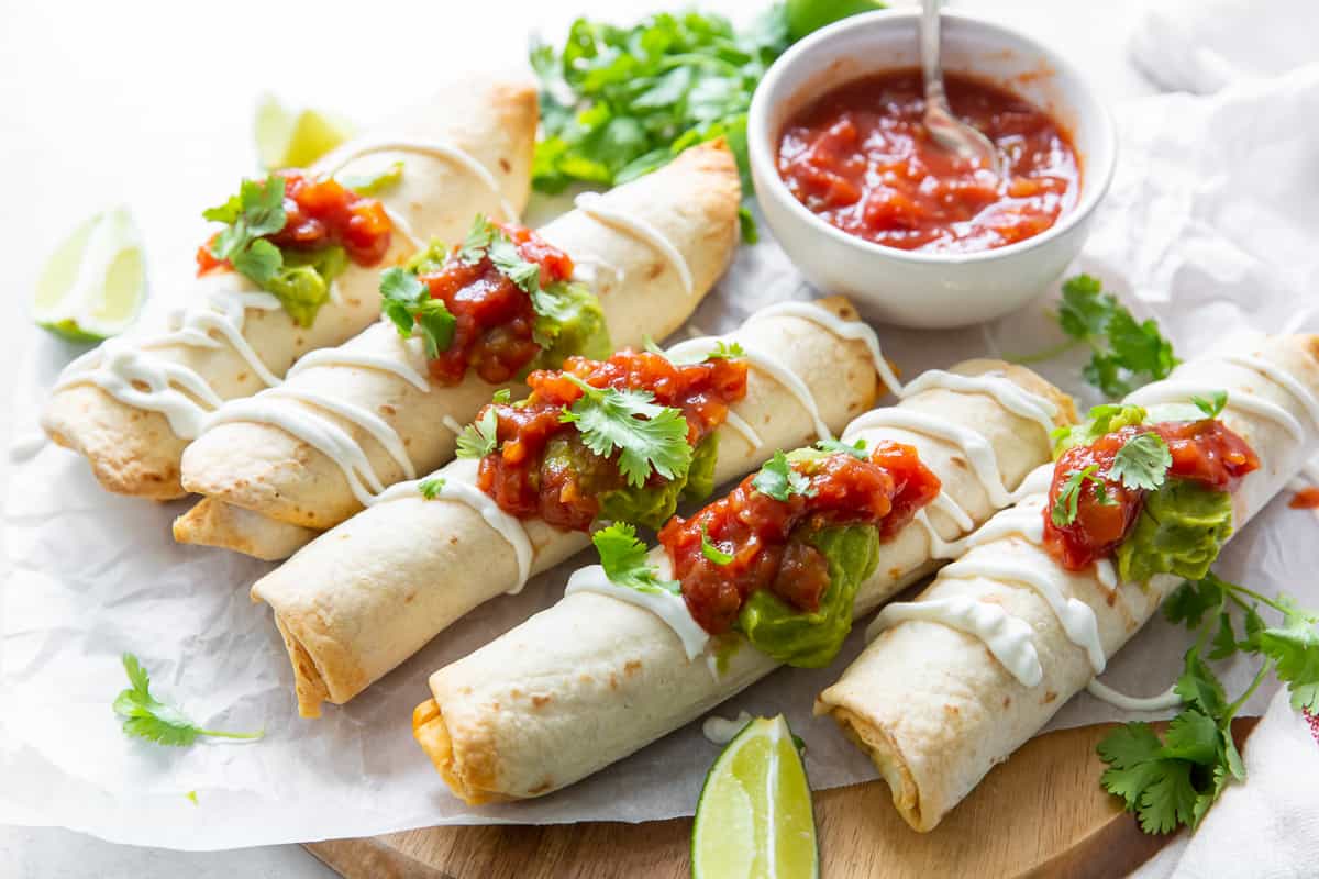 Taquitos on parchment paper next to a bowl of salsa.