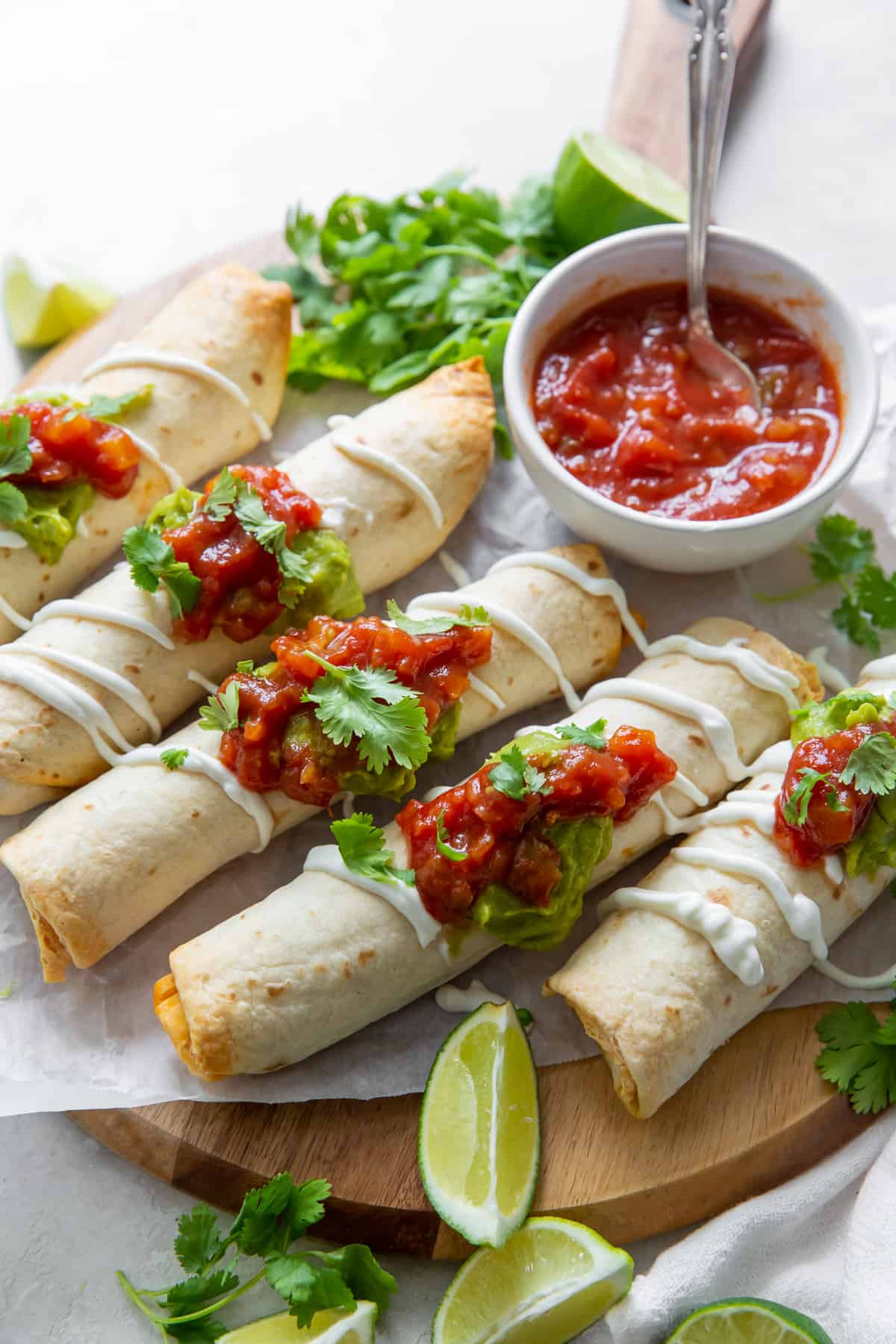Chicken taquitos on a board with a bowl of salsa.