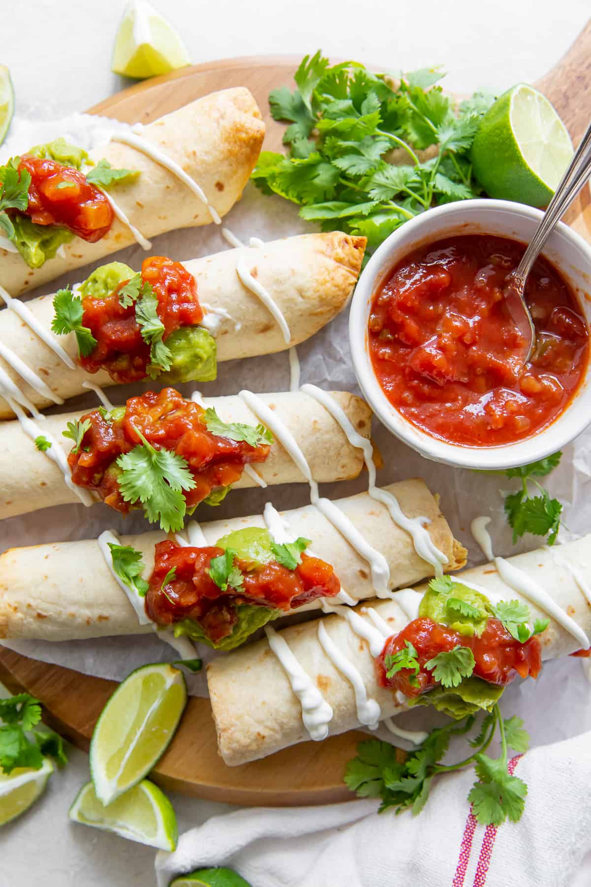 A top down shot of taquitos with salsa and sour cream on a board.