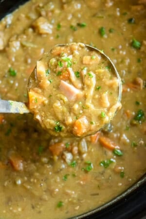 A ladle scooping split pea soup from a slow cooker.