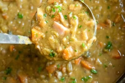 A ladle scooping split pea soup from a slow cooker.