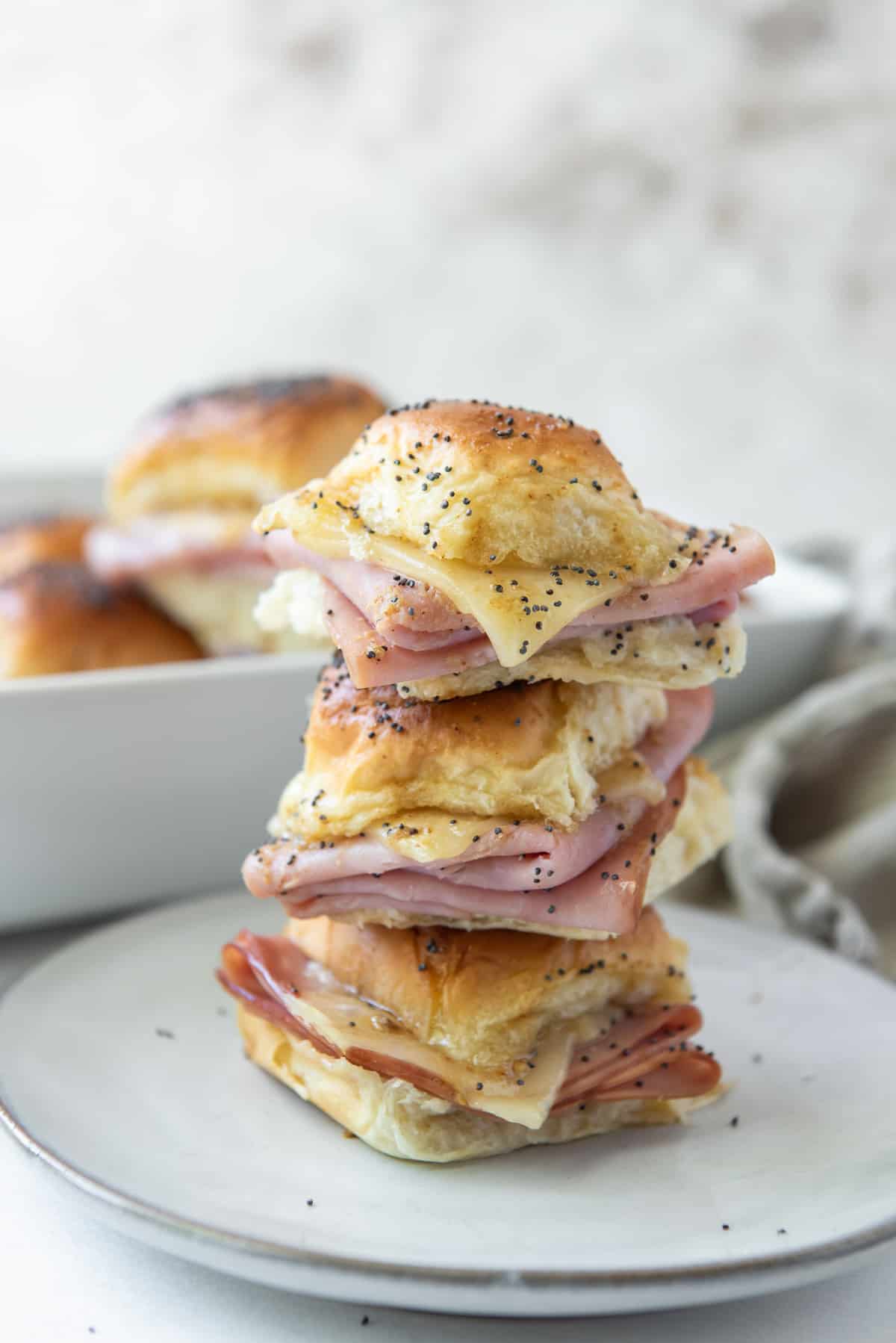 A stack of ham and swiss sliders on a white plate.