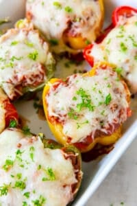 Colored stuffed peppers topped with melted cheese in a white baking dish.