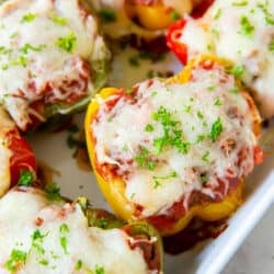 Colored stuffed peppers topped with melted cheese in a white baking dish.