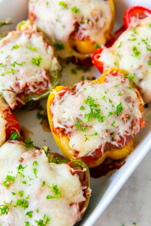 Colored stuffed peppers topped with melted cheese in a white baking dish.