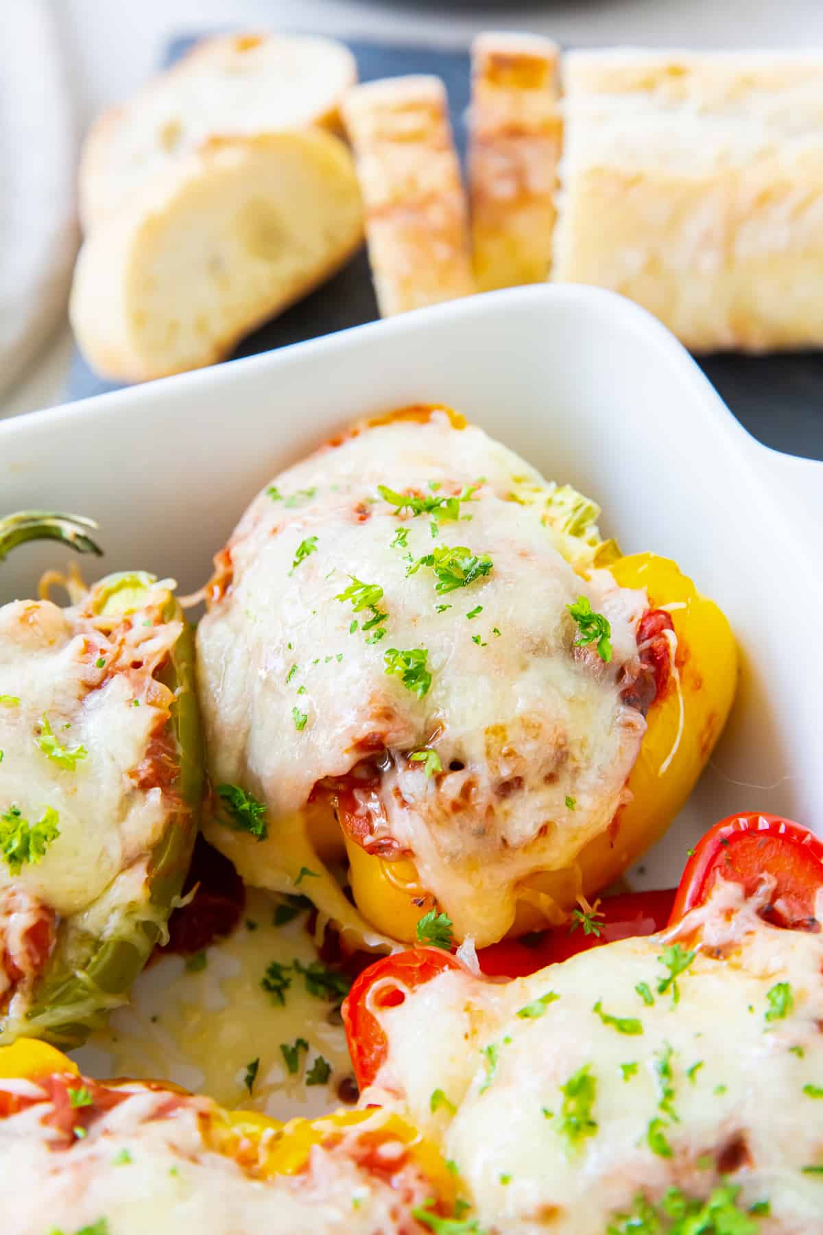 Stuffed peppers in a baking dish next to sliced French bread.