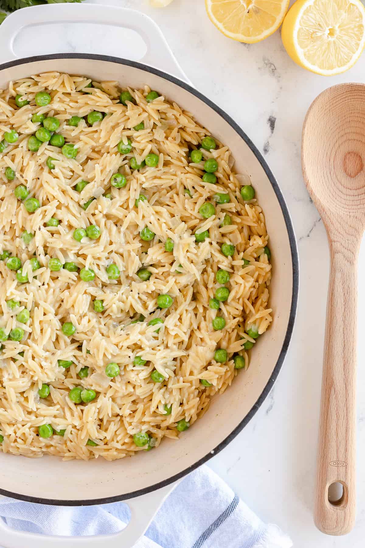 A top down shot of orzo with peas in a white pan.