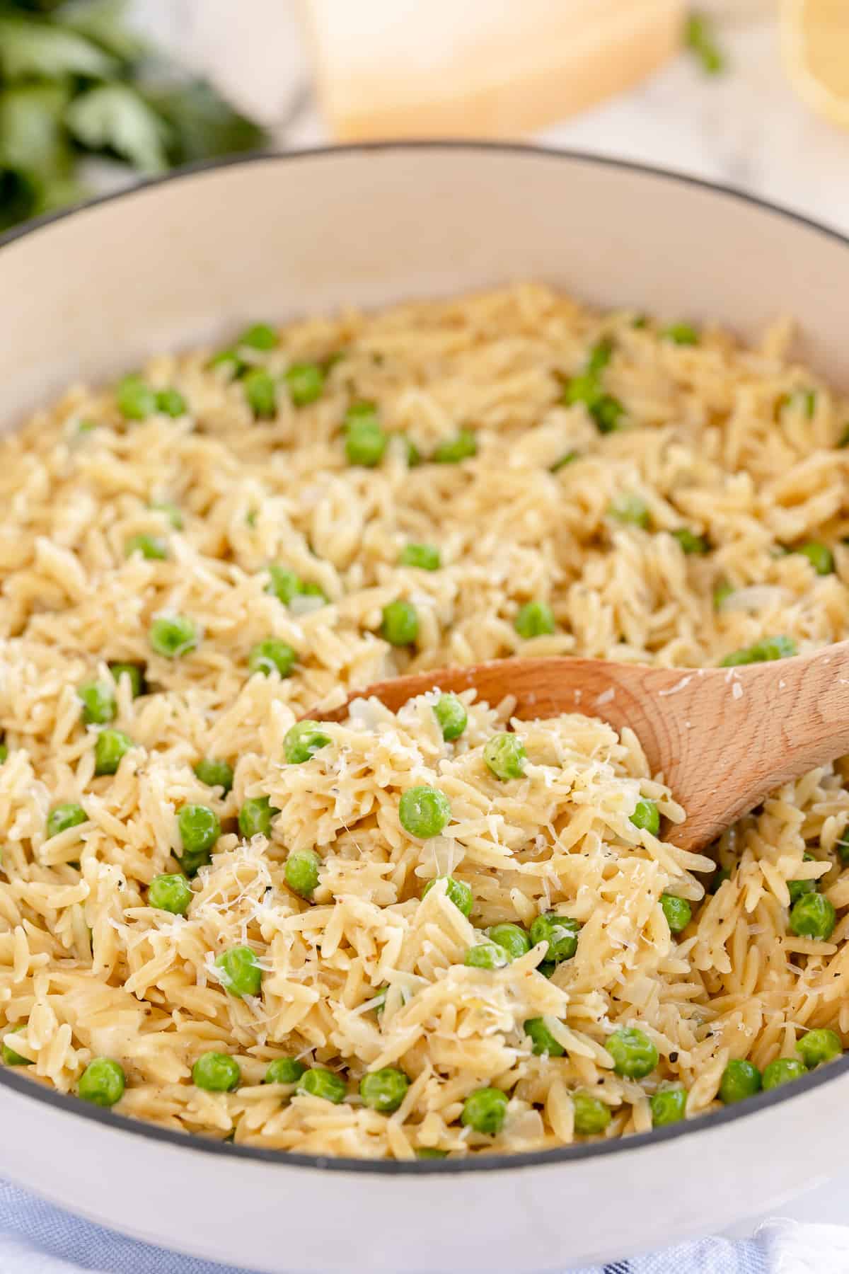 A wooden spoon scoops orzo with peas from a pan.