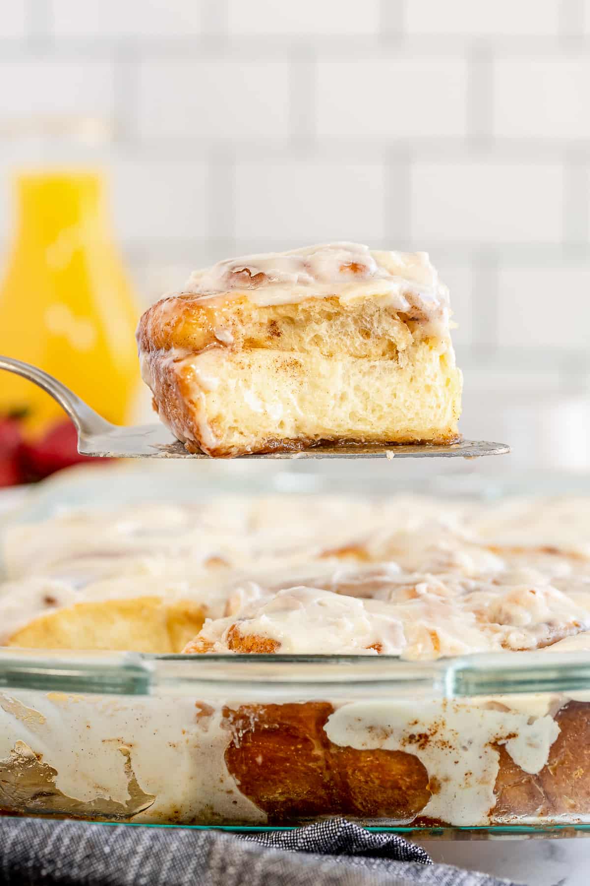 A spatula lifts a cinnamon roll from a baking dish.