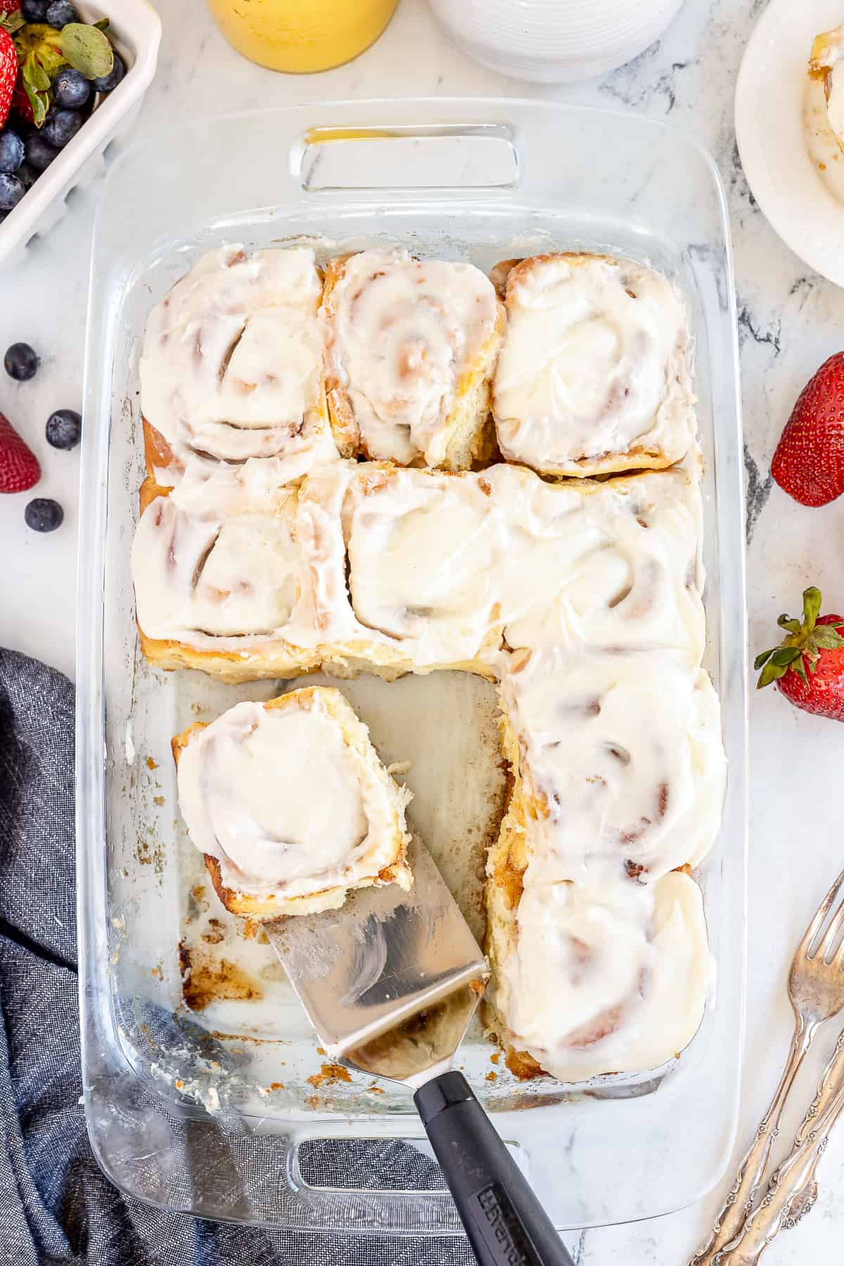 A top down shot of a baking dish of cinnamon rolls with some missing.