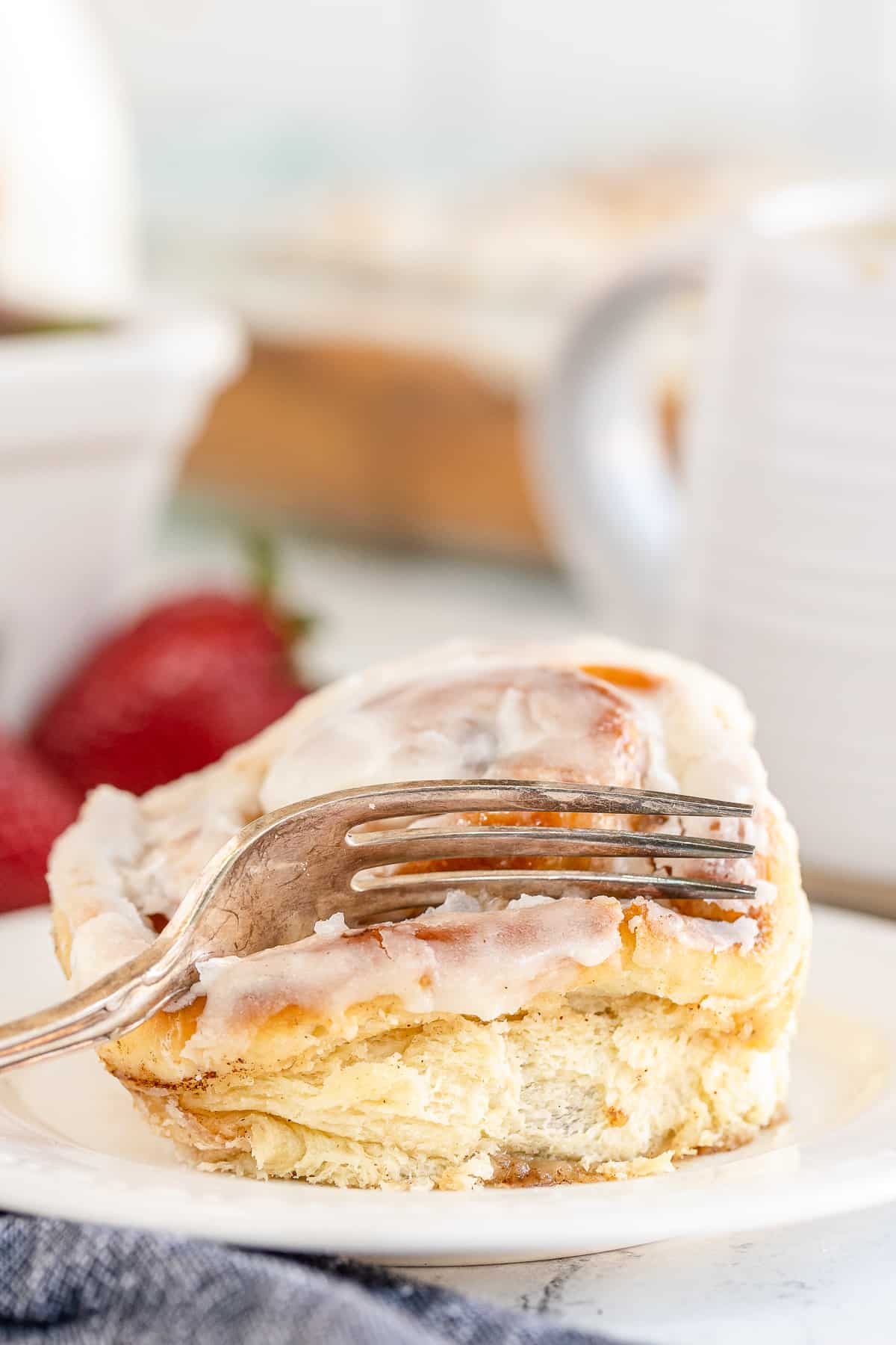 A fork pressing down into a cinnamon roll on  a plate.