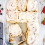 A top down shot of a baking dish full of cinnamon rolls with a spatula.