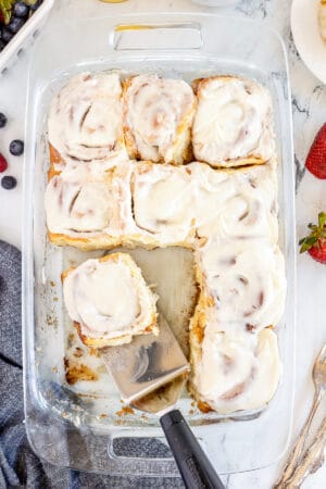 A top down shot of a baking dish full of cinnamon rolls with a spatula.