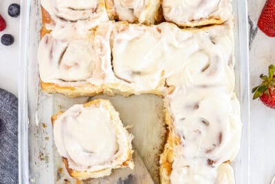 A top down shot of a baking dish full of cinnamon rolls with a spatula.