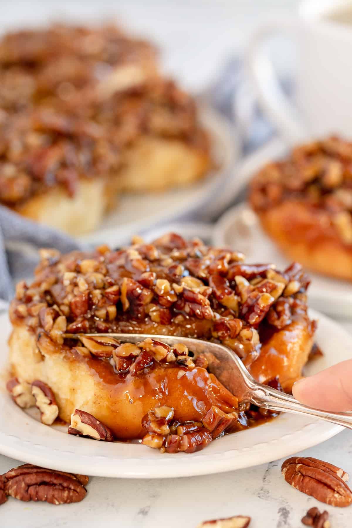 A fork pressing into a sticky bun on a white plate.