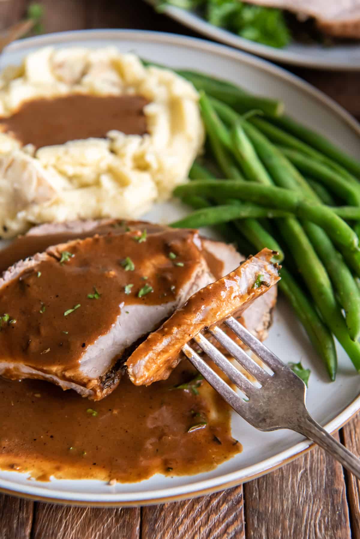 A fork with a bite of pork loin with gravy on a white plate.