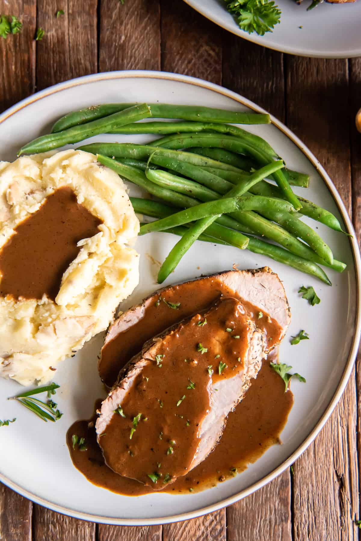 Pork loin roast with gravy on a white plate with potatoes and green beans.