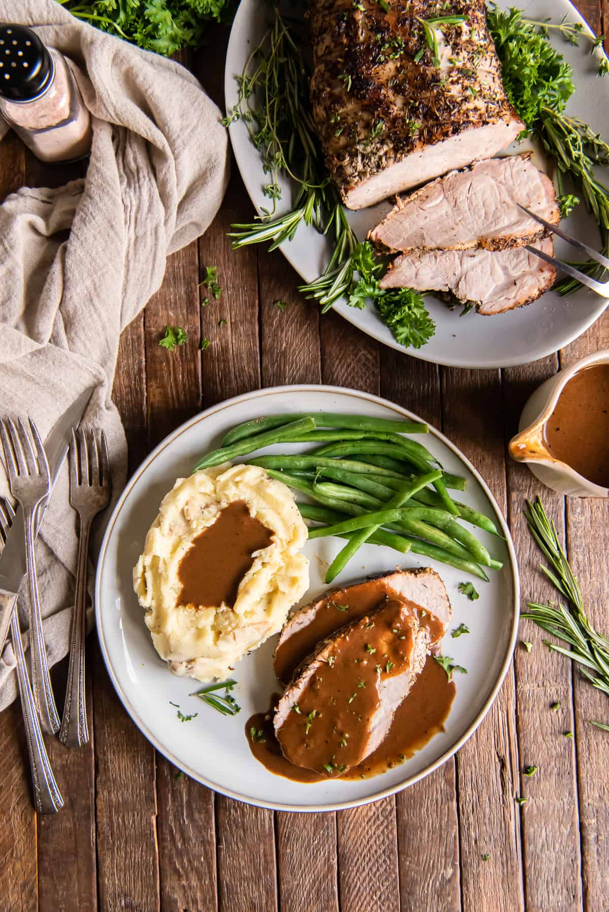 Pork loin roast with gravy on a white plate with potatoes and green beans.