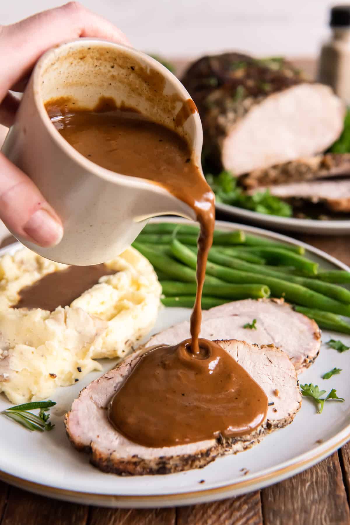 Gravy pouring on sliced pork loin on a plate with mashed potatoes.