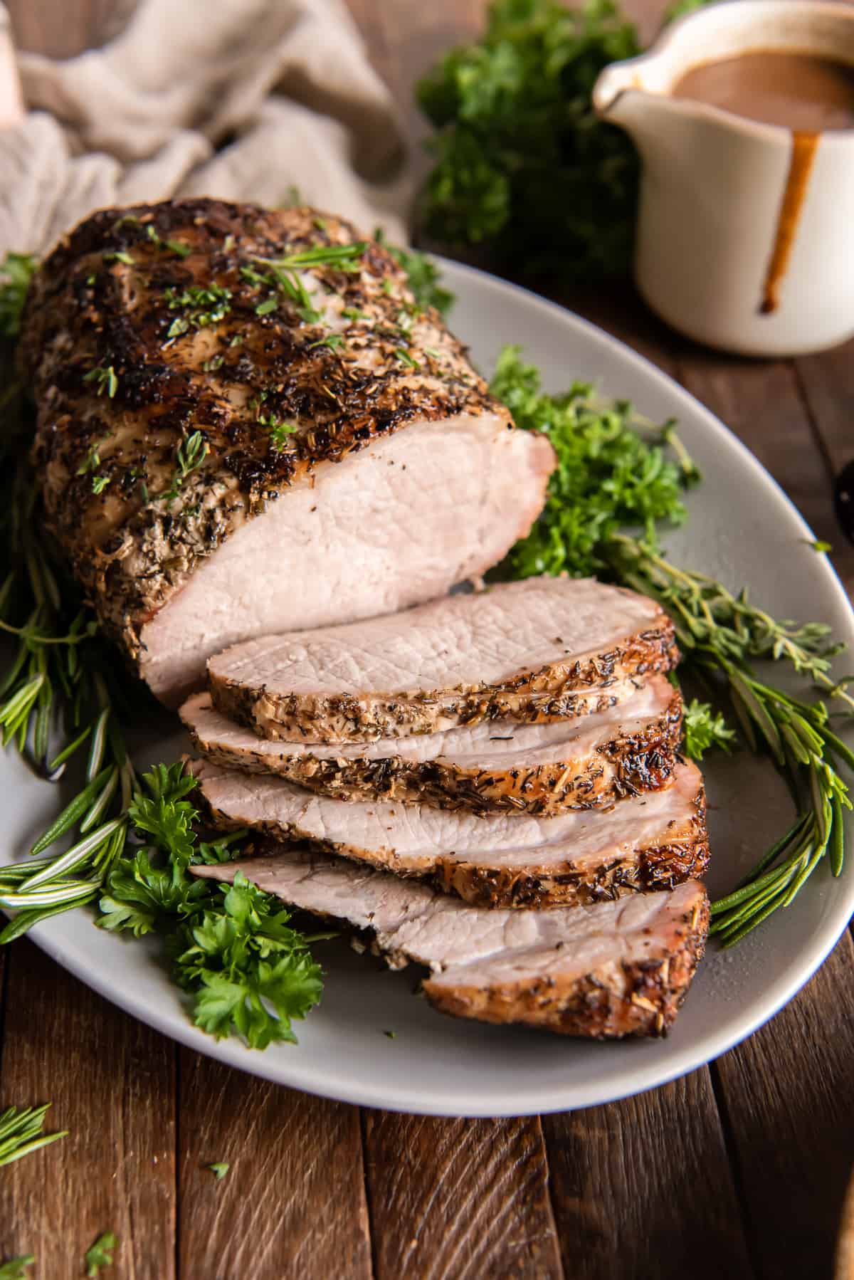 A sliced pork loin roast on a platter with gravy behind it.